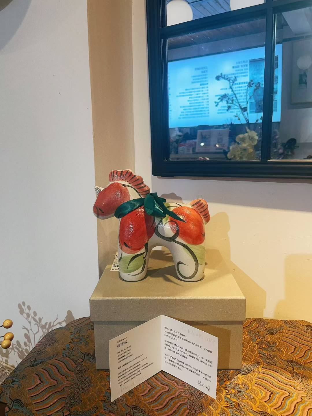 Unicorn-honey porcelain figurine in pink and green on a beige box in room setting